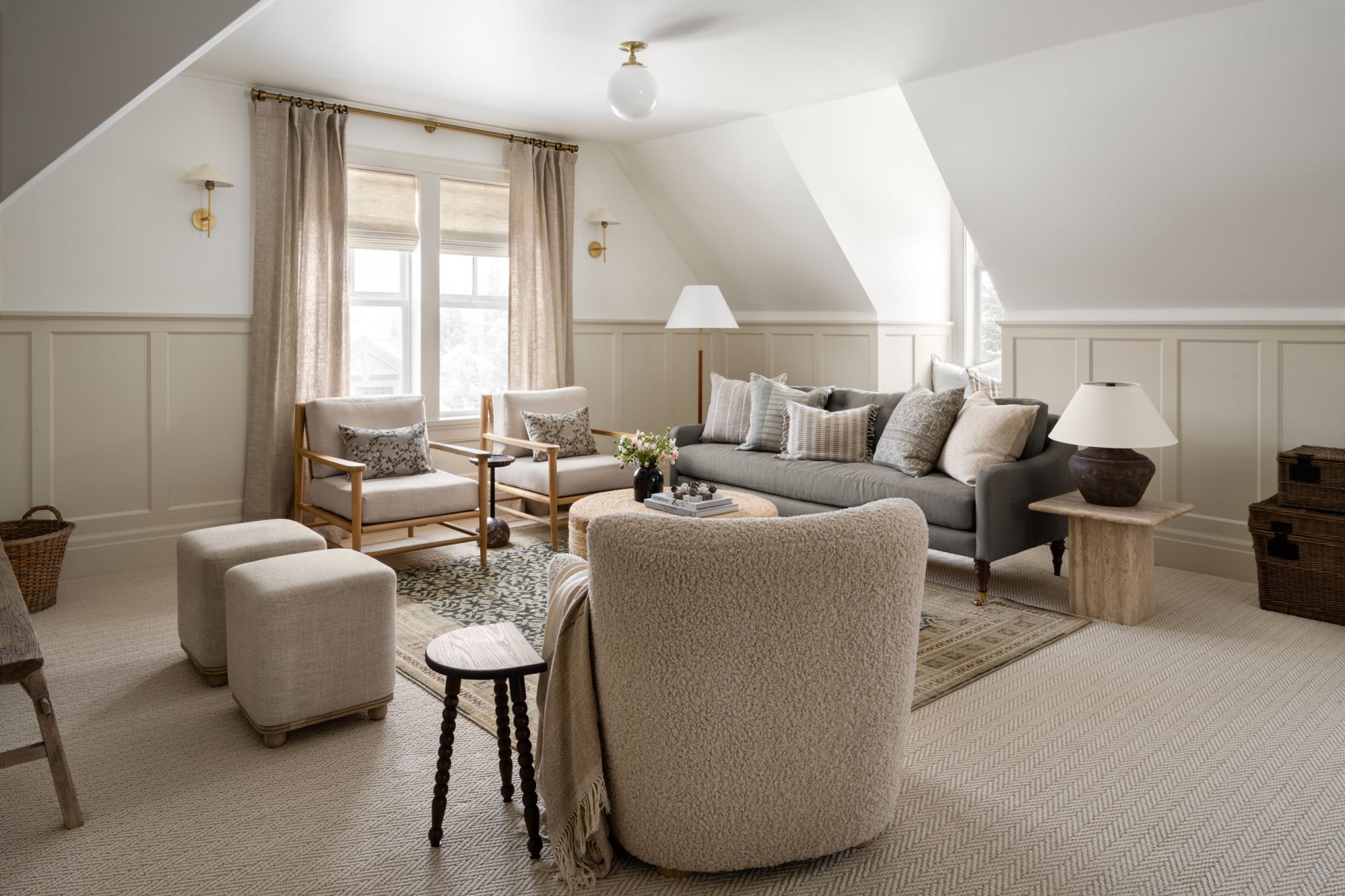 Sala de estar aconchegante com cortinas de tecido bege, poltronas de madeira clara, sofá cinza e mesa de centro redonda em fibras naturais.
