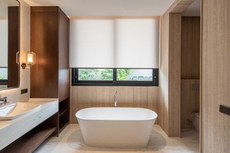 Quarto moderno com persianas automatizadas rolo bege fechadas, cama de casal em tons neutros e parede revestida em madeira.