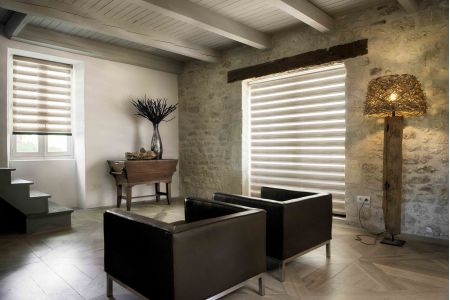 Ambiente elegante com persianas Duo Vision em tons neutros, combinando paredes de pedra e móveis modernos para criar sofisticação e conforto.