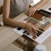 Vista superior detalhada de uma mesa de madeira clara onde mãos manuseiam uma seleção criteriosa de materiais para um projeto de design de interiores. Sobre a mesa, encontram-se amostras de tecidos texturizados, acabamentos em madeira, paletas de cores neutras e um catálogo com a frase "Make Every Space Matter". A cena personifica o suporte técnico e a curadoria de alto padrão oferecidos a arquitetos e clientes, focando na escolha precisa de texturas e materiais que conferem identidade e sofisticação a cada ambiente.